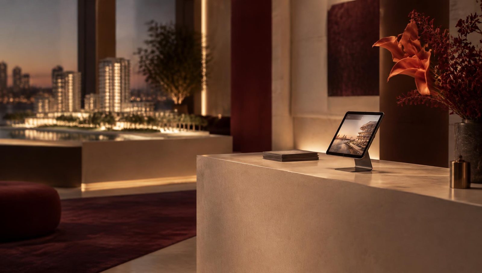A sales gallery at dusk with a tablet check-in stand on a stone counter and a lit architectural model behind it